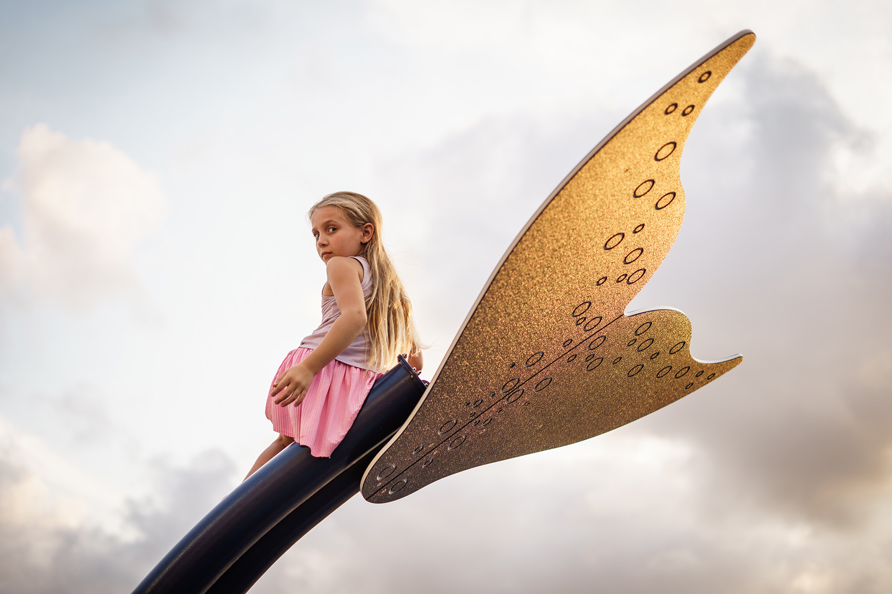 Candid photo of a girl on a whale-tail playground sculpture at sunset in Barcelona