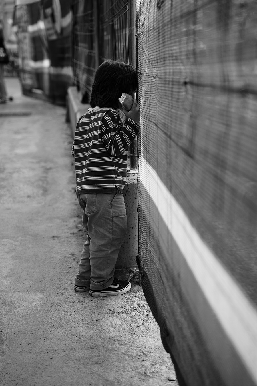Black and white candid photo of a curious child peering through a fence